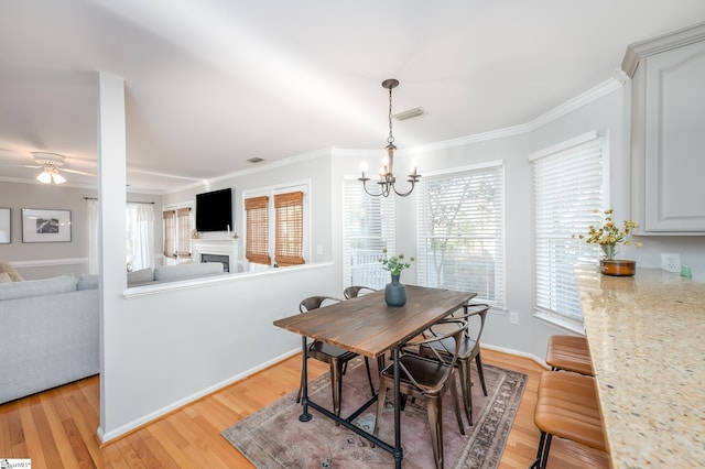 dining area with ornamental molding, light wood finished floors, a fireplace, and visible vents