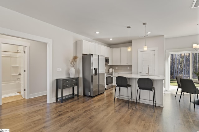 kitchen with white cabinets, a breakfast bar area, hanging light fixtures, stainless steel appliances, and light countertops