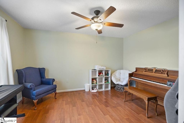 living area with a textured ceiling, light wood-type flooring, a ceiling fan, and baseboards