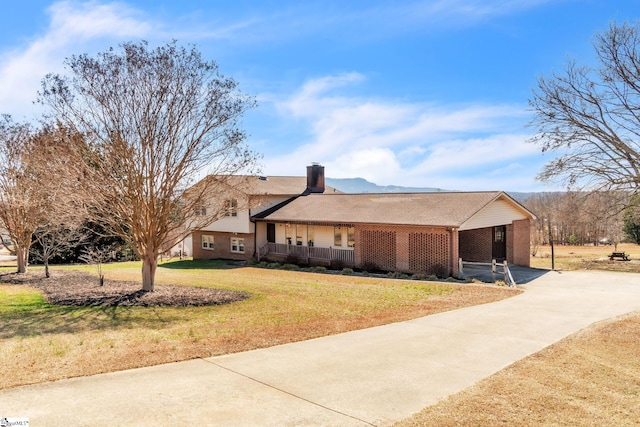 ranch-style house featuring brick siding, a chimney, covered porch, driveway, and a front lawn