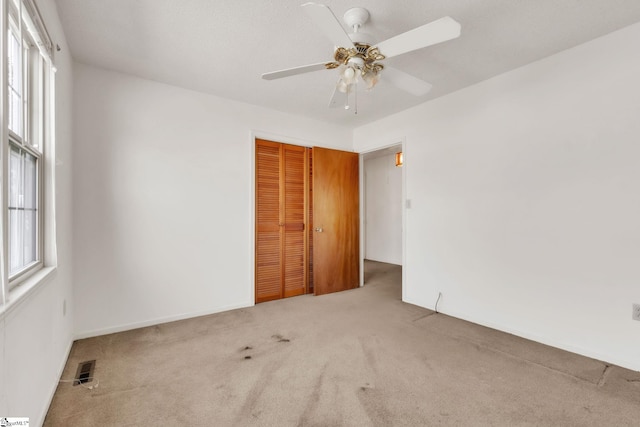 empty room featuring a healthy amount of sunlight, carpet, visible vents, and ceiling fan