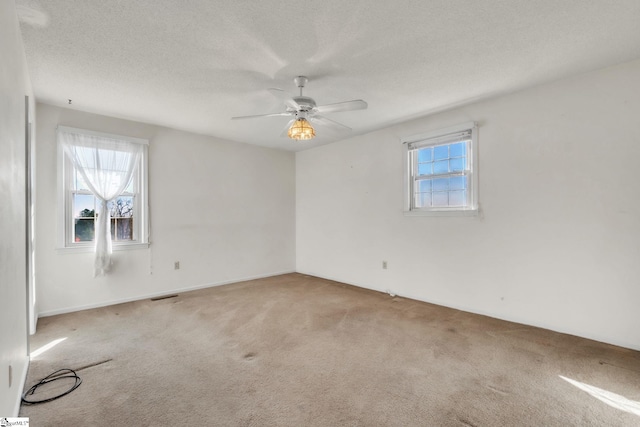 empty room featuring carpet floors, a wealth of natural light, visible vents, and a textured ceiling