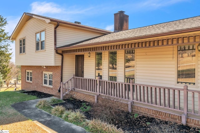 exterior space with a porch, brick siding, a shingled roof, and a chimney