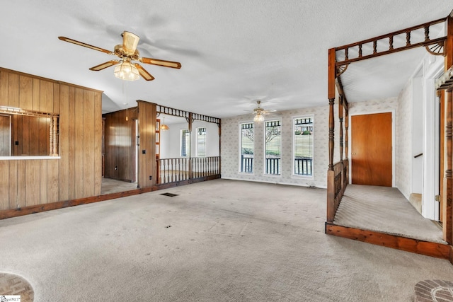 unfurnished living room with visible vents, ceiling fan, a textured ceiling, carpet flooring, and wood walls