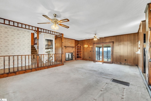 unfurnished living room with a textured ceiling, carpet floors, a fireplace, visible vents, and a ceiling fan