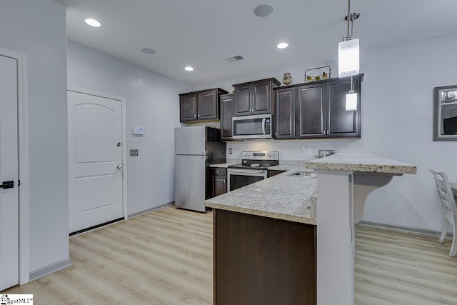 kitchen with pendant lighting, stainless steel appliances, visible vents, a peninsula, and a kitchen bar