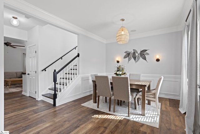 dining room featuring dark wood-type flooring, a wainscoted wall, crown molding, and stairs