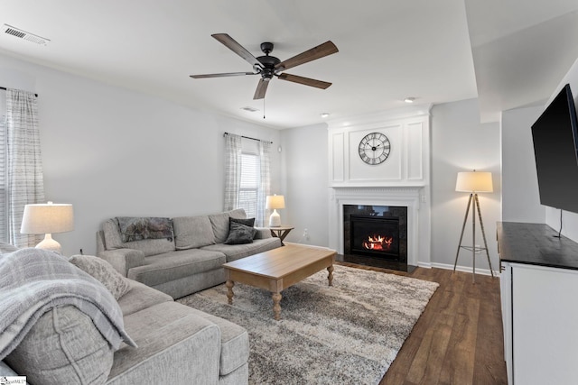 living room with dark wood-style floors, ceiling fan, visible vents, and a large fireplace