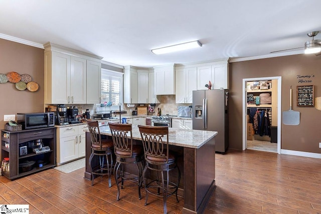 kitchen featuring dark wood finished floors, a kitchen island, light stone countertops, stainless steel appliances, and white cabinetry