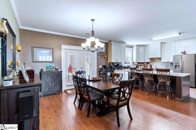 dining space featuring light wood finished floors, a notable chandelier, crown molding, and french doors