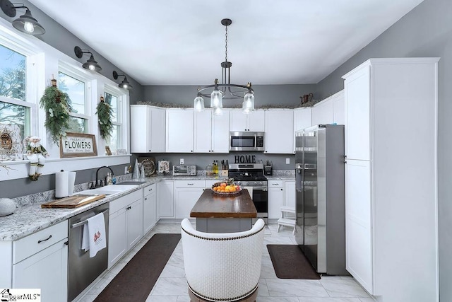 kitchen featuring decorative light fixtures, appliances with stainless steel finishes, white cabinetry, a kitchen island, and a sink