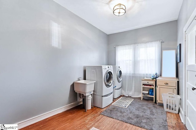 laundry room with laundry area, a sink, baseboards, light wood-type flooring, and washing machine and clothes dryer