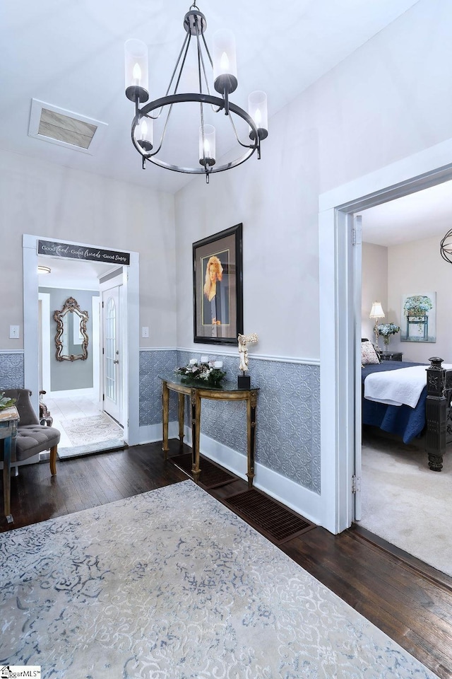 foyer entrance with an inviting chandelier, visible vents, dark wood-type flooring, and wainscoting