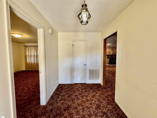 hall with a textured ceiling, carpet, visible vents, and baseboards