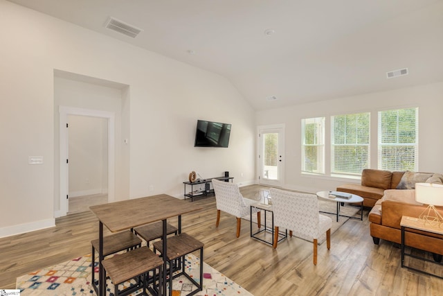 living room featuring light wood-type flooring, lofted ceiling, visible vents, and baseboards