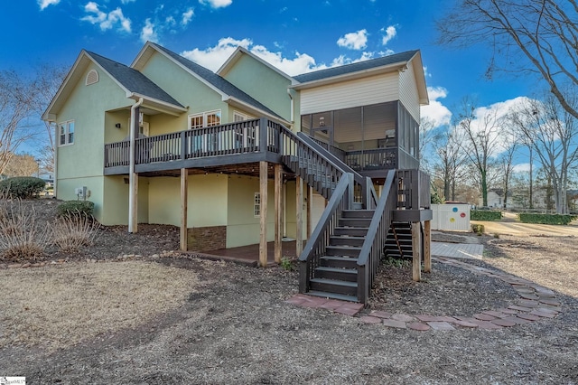 rear view of house with a sunroom, stairs, a deck, and stucco siding