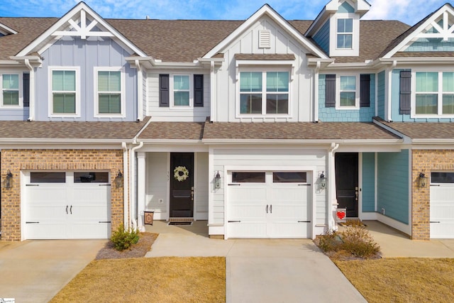 townhome / multi-family property with driveway, a garage, a shingled roof, board and batten siding, and brick siding