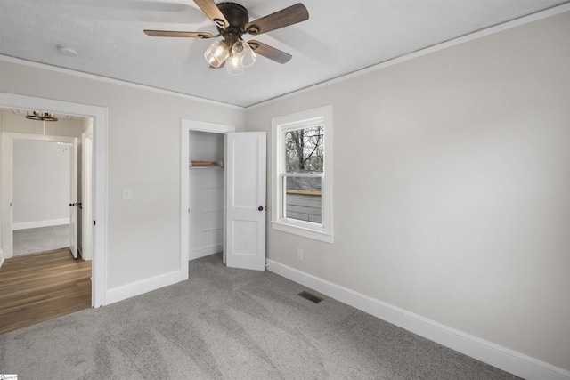 unfurnished bedroom featuring baseboards, visible vents, carpet, crown molding, and a closet