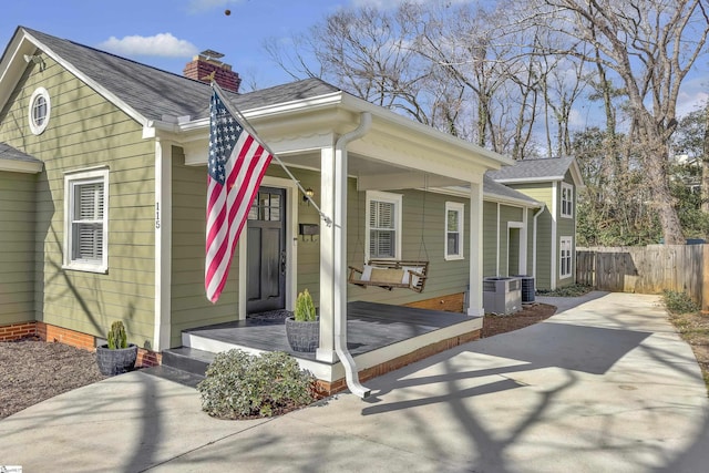 view of front of house featuring a chimney, roof with shingles, fence, a porch, and central AC