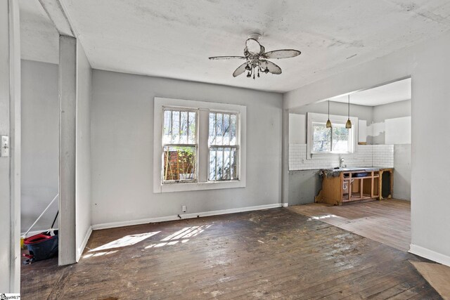 unfurnished living room featuring dark wood-style floors, a ceiling fan, and baseboards