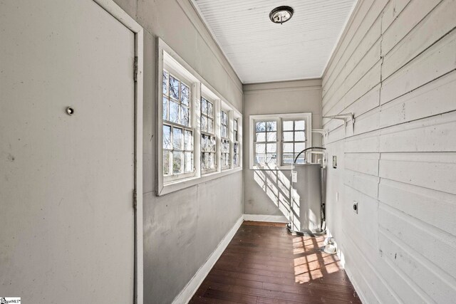 hall featuring dark wood-style floors, wood walls, gas water heater, and baseboards