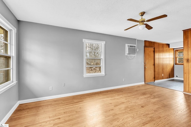 empty room with a textured ceiling, a ceiling fan, baseboards, an AC wall unit, and light wood finished floors