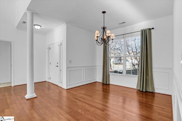 unfurnished dining area featuring decorative columns, visible vents, wood finished floors, an inviting chandelier, and a decorative wall