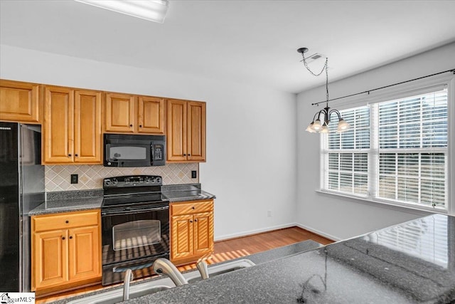 kitchen featuring decorative backsplash, light wood-style floors, brown cabinets, black appliances, and pendant lighting