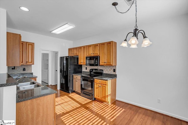 kitchen featuring brown cabinetry, dark countertops, decorative light fixtures, black appliances, and a sink