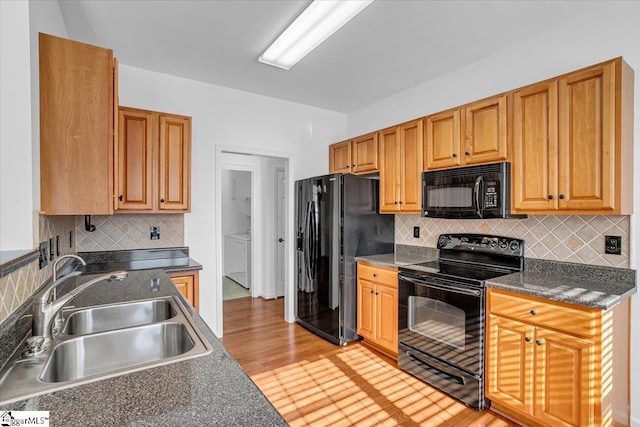 kitchen with brown cabinets, dark countertops, a sink, separate washer and dryer, and black appliances