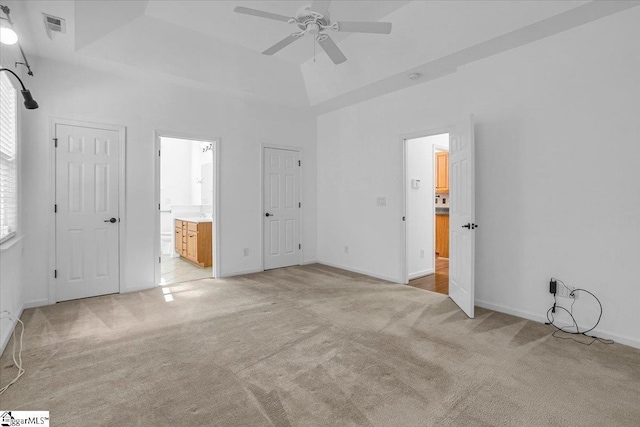 unfurnished bedroom featuring a raised ceiling, light colored carpet, visible vents, a towering ceiling, and ensuite bathroom