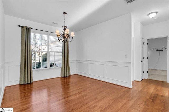 unfurnished dining area featuring wainscoting, wood finished floors, visible vents, and a notable chandelier