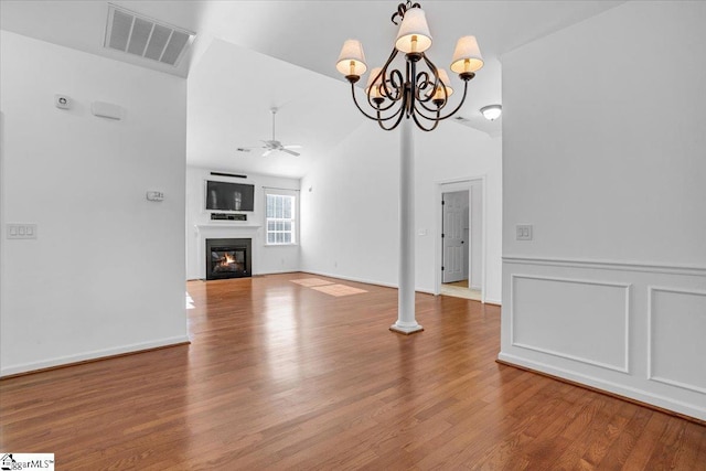 unfurnished living room with lofted ceiling, ceiling fan with notable chandelier, wood finished floors, visible vents, and a glass covered fireplace