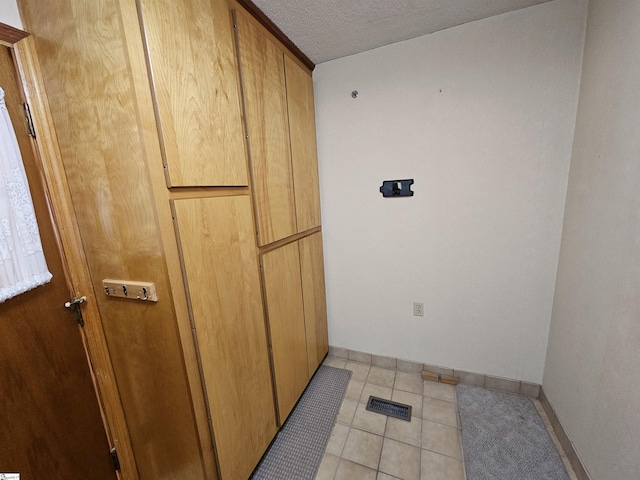 interior space featuring laundry area, a textured ceiling, baseboards, and light tile patterned floors