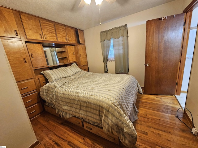 bedroom with a textured ceiling, ceiling fan, dark wood-type flooring, and baseboards