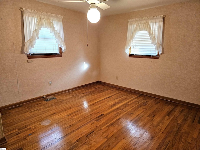 spare room with a ceiling fan, wood finished floors, visible vents, and baseboards