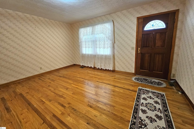 entryway featuring wood finished floors, baseboards, and wallpapered walls