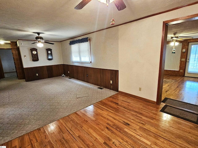 unfurnished living room featuring a healthy amount of sunlight, a textured ceiling, wood finished floors, and wainscoting