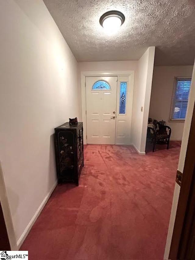 doorway to outside featuring carpet, baseboards, and a textured ceiling