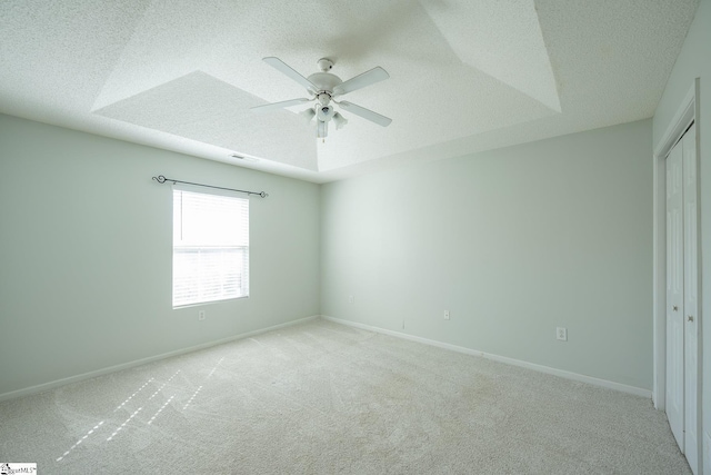 empty room with a raised ceiling, light colored carpet, a textured ceiling, and baseboards