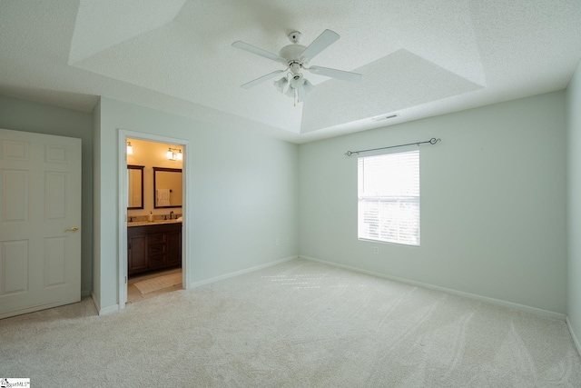 unfurnished bedroom with a raised ceiling, light colored carpet, visible vents, a textured ceiling, and baseboards