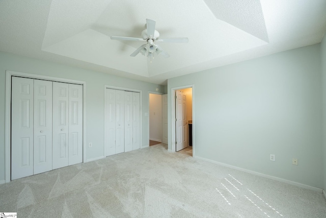 unfurnished bedroom with baseboards, light colored carpet, a tray ceiling, a textured ceiling, and multiple closets