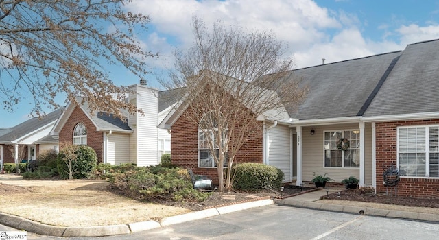 view of front of property with uncovered parking, brick siding, and roof with shingles