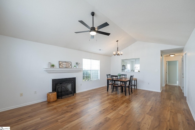 dining room with baseboards, lofted ceiling, wood finished floors, a fireplace, and ceiling fan with notable chandelier