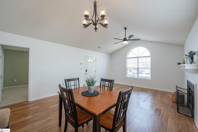 dining room with a fireplace, a ceiling fan, baseboards, vaulted ceiling, and dark wood finished floors