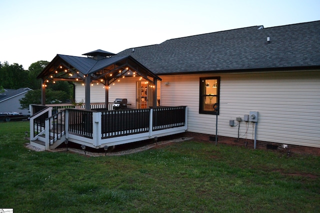 back of property with a yard, a wooden deck, a shingled roof, and crawl space