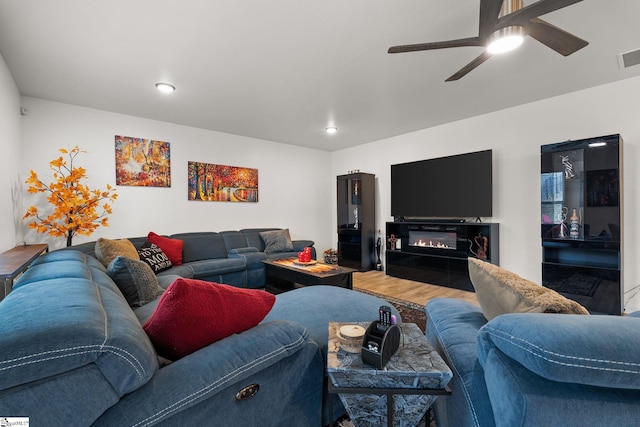 living area with visible vents, a glass covered fireplace, ceiling fan, wood finished floors, and recessed lighting