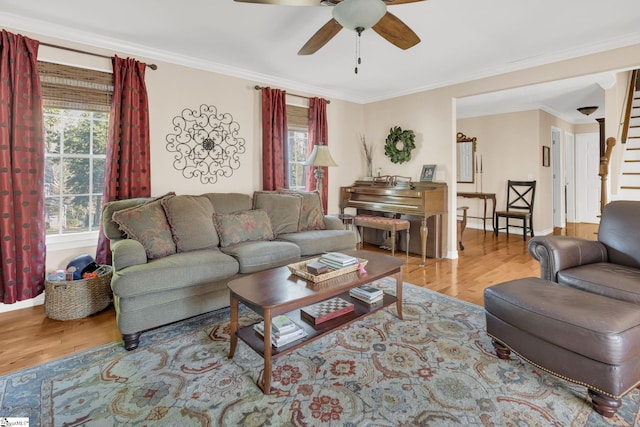 living area featuring light wood finished floors, stairs, ornamental molding, and a ceiling fan