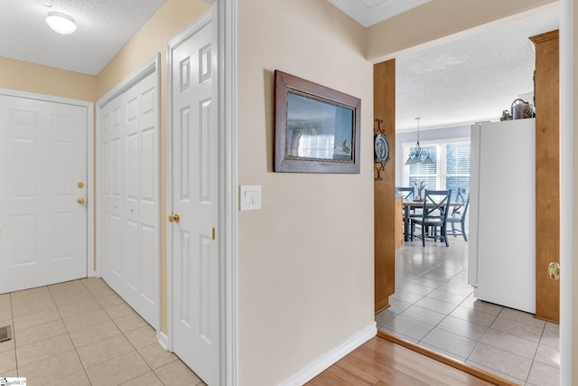 corridor with a textured ceiling, baseboards, and light tile patterned floors