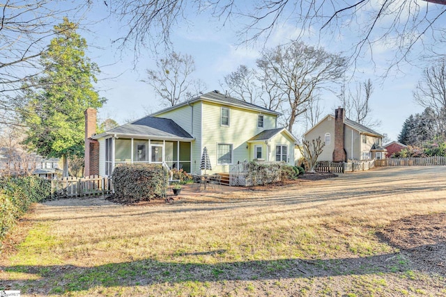 view of front of home featuring a sunroom, fence, a chimney, and a front lawn